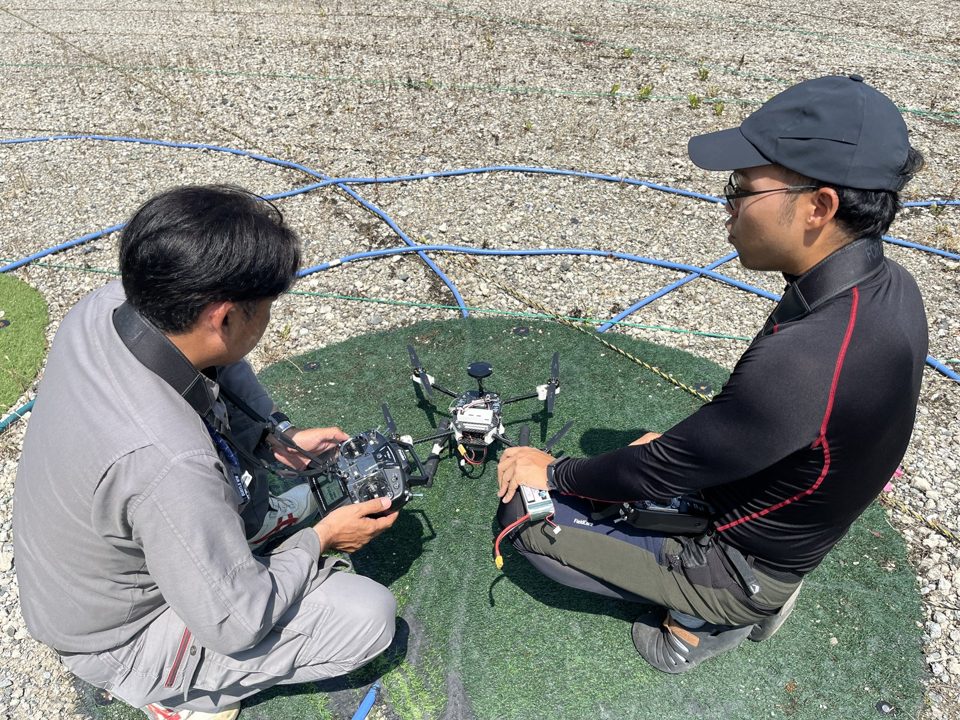 講師が受講生の横について送信機の操作を指導する様子